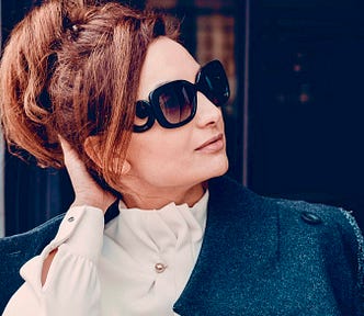 An attractive middle-aged woman in sunglassees and wearing black looks off to the side