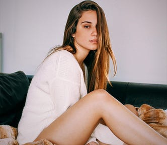 girl with long brown hair wearing white top sitting on bed