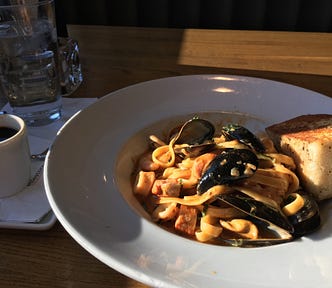 Seafood pasta with a piece of bread on the side. And a coffee next to the dish.