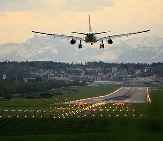 Plane about to land on runway, snowy mountains in background