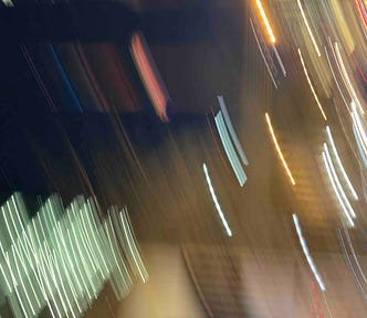 Abstract night scene with colorful light streaks — white, yellow, red, and blue — suggesting motion and energy in an urban setting.