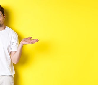 A clueless looking man in a white t shirt, shrugging and looking puzzled as if he has no idea what is going on. Bright yellow background.
