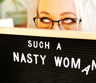Author holds sign board that reads “Such a nasty woman.” She is rolling her eyes.