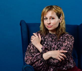 An attractive woman sitting in a comfortable chair, with her arms crossed in a guarded posture.