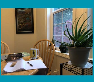 A warmly lit kitchen with the blank page of a notebook, houseplants, and the bedraggled raven coffee cup.