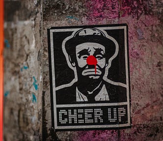 A black and white sticker of sad clown with a red nose and the caption “cheer up”