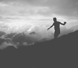 silhouette of man balancing on sloped hillside with cloudy sky in background