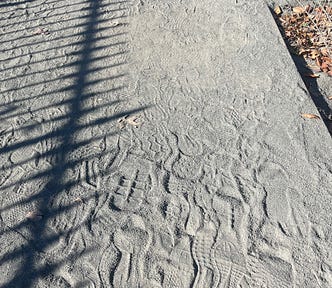 Hundreds of treads on the gravelly path of the Reservoir in NYC. It’s a sunny day and you can see a shadow of the railing around the water.