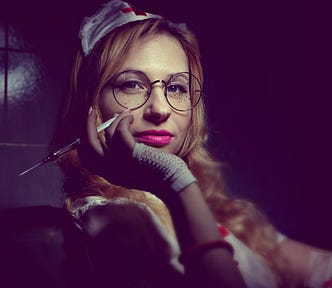 Image of a woman with an old-fashioned nurse’s cap on her head, resting her chin in her hand and in her hand she holds a syringe. She wears glasses and looks straight into the camera with a slight smile around her red lips.