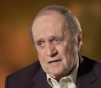 Bob Newhart in an interview, with his piercing blue eyes, everyman face and wearing a black jacket with yellow shirt.