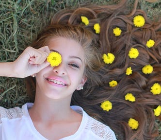 Happy teen lying on a grassy field and wearing yellow flowers in her hair