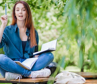 Girl sitting cross-legged holding books on her lap and a pen in her right hand