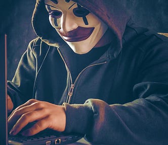 Hacker with a hoodie and evil clown mask typing on a laptop