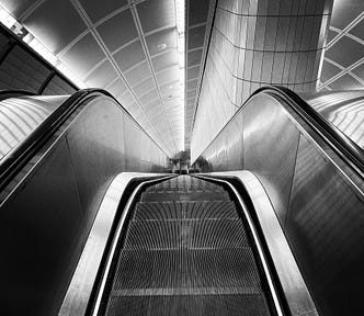 A black and white photo looking down a steep, long escalator.