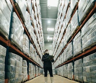 A worker stands in between shelves in a large warehouse.