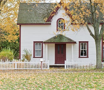 Repairing, upgrading, and staging a home for sale. Photo of a single family home with white picket fence. Autumn leaves are blanketing the front lawn.