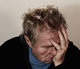An older man with disheveled hair holding his face in his hand