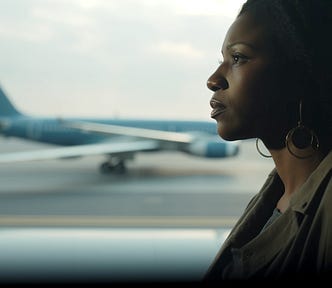 A photo of Sarah, a dark skinned middle age woman watching airplanes coming and going while waiting for her connection.