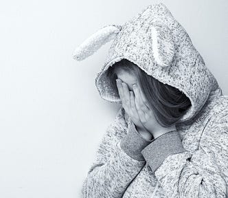 Monochrome image of a person wearing a hoodie with rabbit ears, hands held before their face.