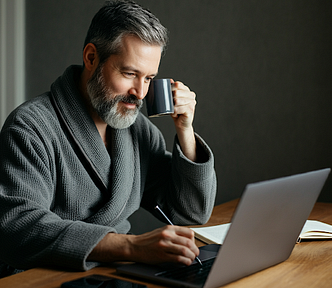 A writer with coffee using a pen to write on his computer.