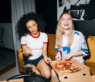 Two women eating pizza and drinking wine.