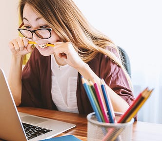 A woman holding a pencil to her mouth and looking at her laptop screen