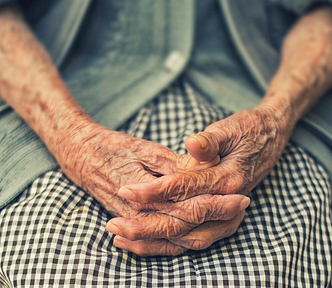 The hands of an old person clasped together on their lap
