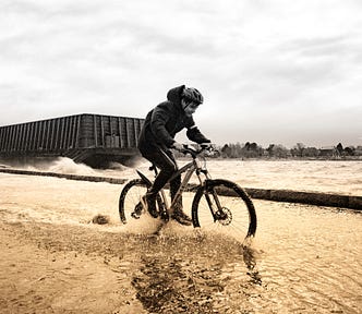 A man pedals a bike through ankle-deep water.