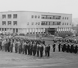 Black-and-white photograph of officials standing in lines outside buildings.