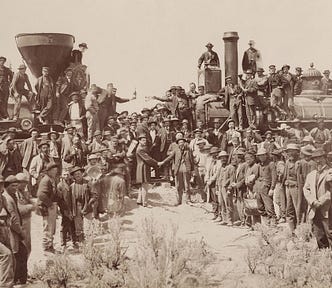 Sepia photo of men standing with two locomotives on the day the transcontinental railroad was opened