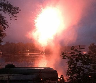 a nighttime photo of fireworks over a lake. Very bright pink flare of the pyrotechnics exploding