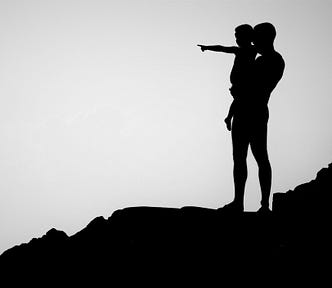 silhouette of man standing on rocky hillside holding small child in his arms