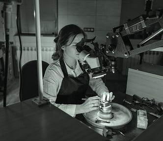 A woman is seated in a lab and is looking through a microscope.