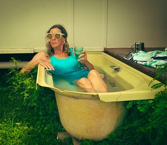 A woman relaxing in an old bathtub outdoors, holding a glass of wine