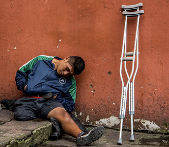 Crippled man, sitting leant over, new crutches.