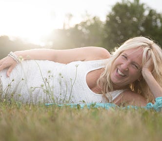 Liz Porter laying on her side in the grass in a white sleeveless dress laughing