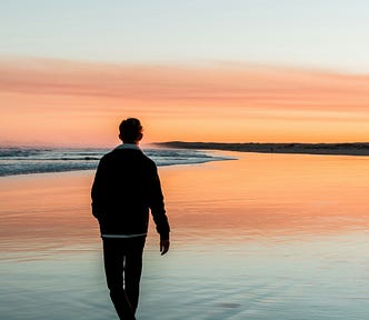 man walking alone on beach at sunrise reflecting anxiety and mental health