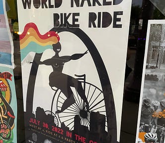 In the poster, a woman with long, rainbow colored long hair is riding naked on a bike.