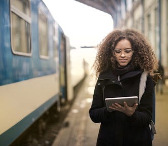 A young woman on a railway station, looking at her iPad.