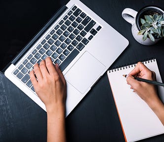 An editor working on a laptop and notebook.
