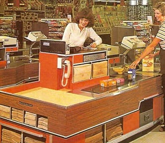 Vintage grocery store. Cashier wearing brown pants and vest over a brown striped shirt. Customer wearing a white long sleeved shirt writing a check. Store is very orange and brown paneling. Possibly a Skaggs.