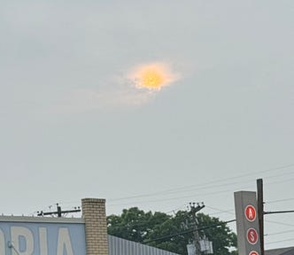 Photo of a faint sun peeking out from gray clouds.