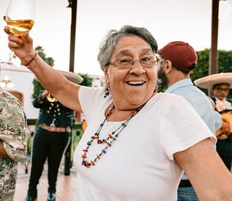 An older woman with a quirky smile lifts a glass of wine.