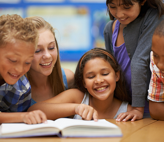 Group of students smiles while reading with their teacher.