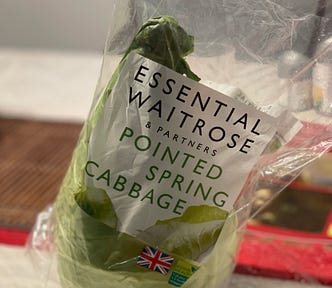 A pointed green cabbage wrapped in its store packaging.