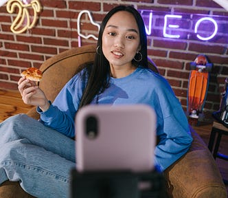 A Woman Recording Herself with a Smartphone while eating a slice of pizza
