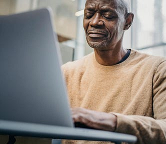 Senior man focused on working remotely using laptop in urban office.