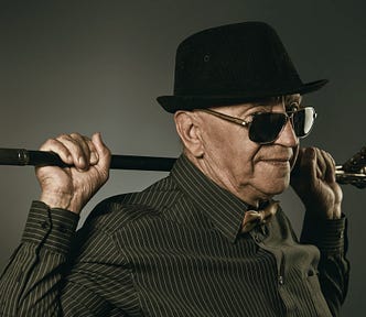 Stylish older man in hat and sunglasses holding cane across shoulders