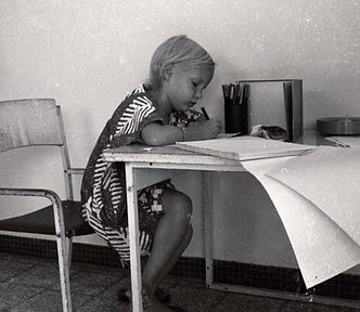 picture of the author as a six- or seven-year old sitting a terrace table in the Ivory Coast, writing or drawing…