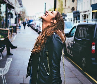 happy smiling girl with long brown hair wearing black leather jacket looking up to the sky